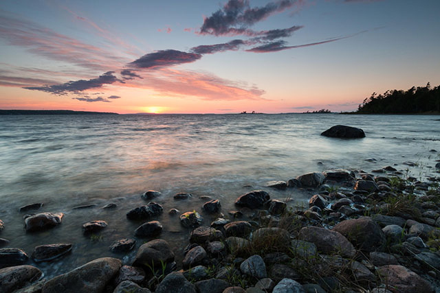 A sunset over a calm lake with a rocky shoreline.