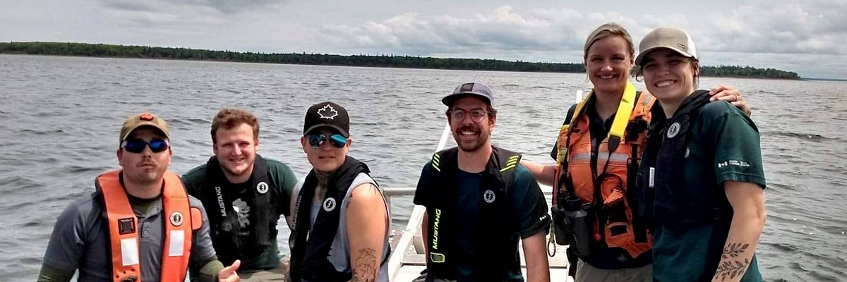 Six people wearing personal floatation devices sit on a boat, smiling and posing comfortably together for the camera.
