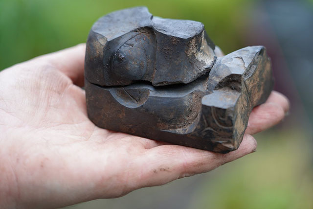 A hand holds a dark coloured, palm-sized rock carved with intricate patterns.