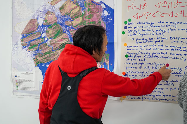 A person places a round sticker on chart paper covered in notes in Inuktitut and English, hung on a wall next to a map.