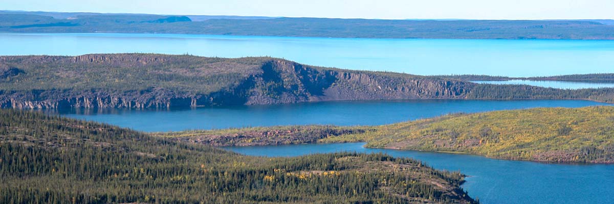 A panoramic view of multiple bodies of calm water, divided by rocky heads of land, covered with coniferous forests or tundra vegetation.