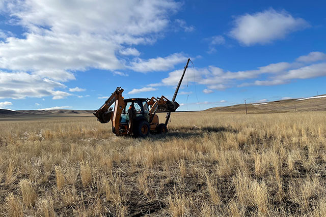 A heavy piece of construction equipment removes a power line pole from the grasslands.